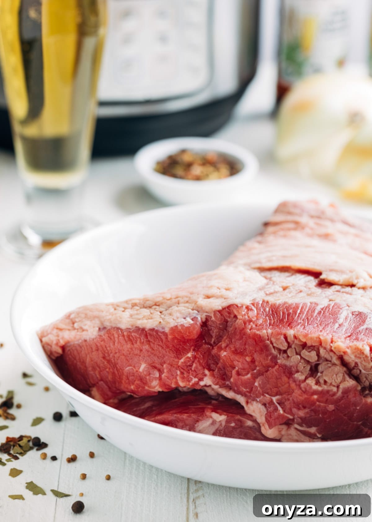 uncooked corned beef in a white bowl with a glass of beer and an instant pot in the background