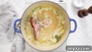 Overhead photo of a pot of split pea soup simmering with a ham bone, bay leaf, and thyme.