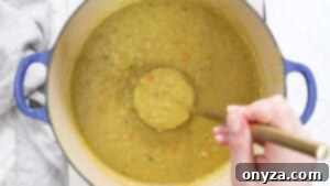 Overhead photo of a pot of split pea soup with a ladle, showing its thick, creamy texture and chunks of ham.