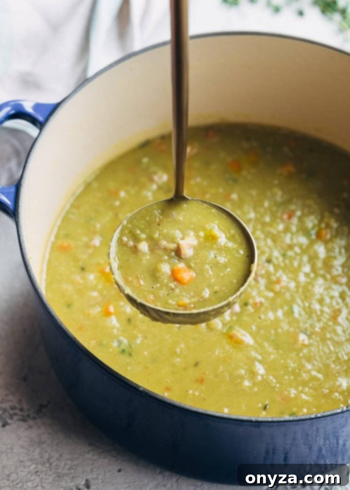 A ladleful of hearty split pea soup with chunks of ham, served in a rustic blue cast iron pot.