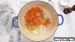 Overhead photo of a Dutch oven containing diced onion, celery, and carrots sautéing in butter.