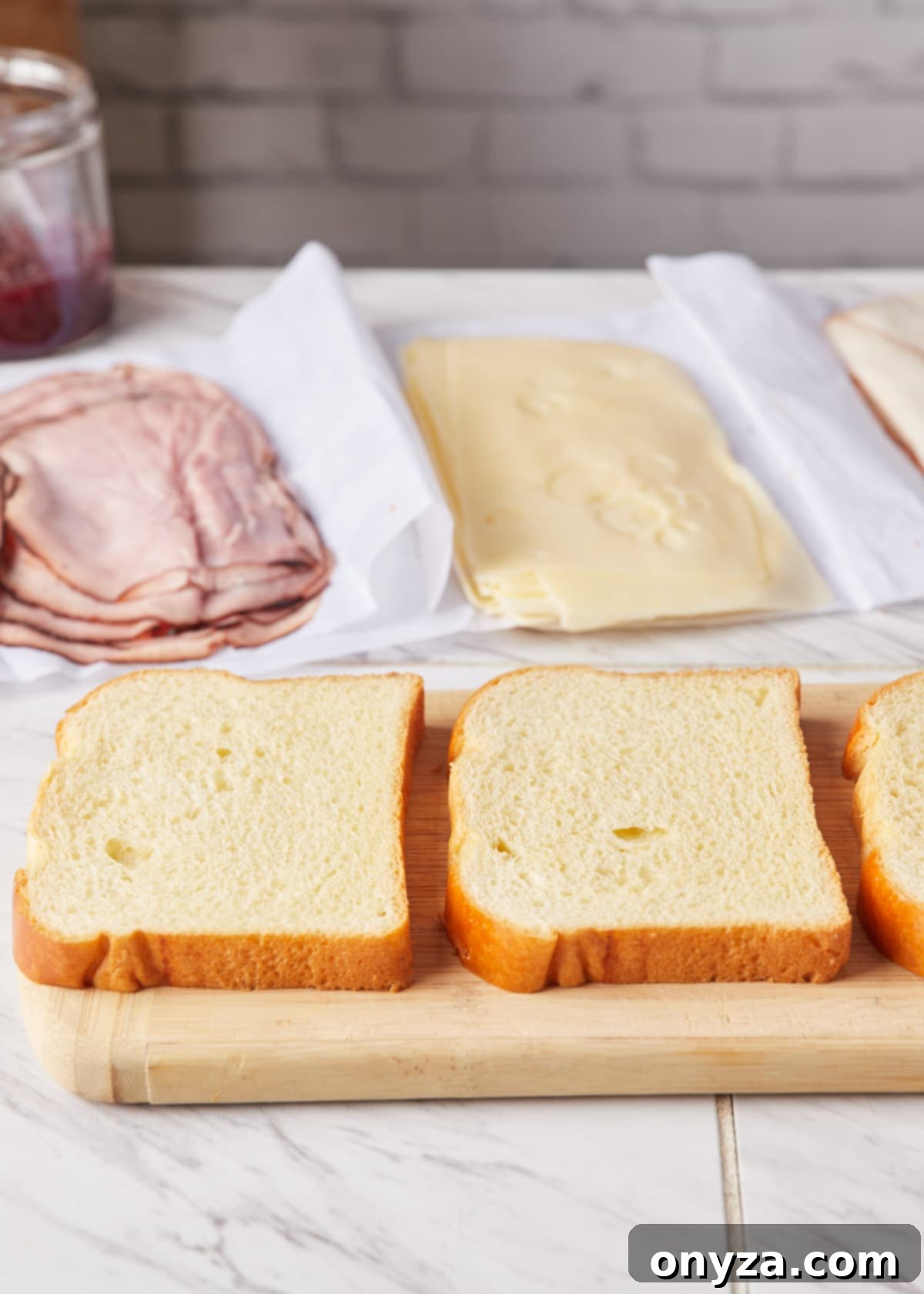 Sweet and Savory Golden Delight 3 Slices of white bread on a wooden cutting board, in front of sliced ham, Swiss, and turkey on deli paper, showcasing Monte Cristo ingredients.