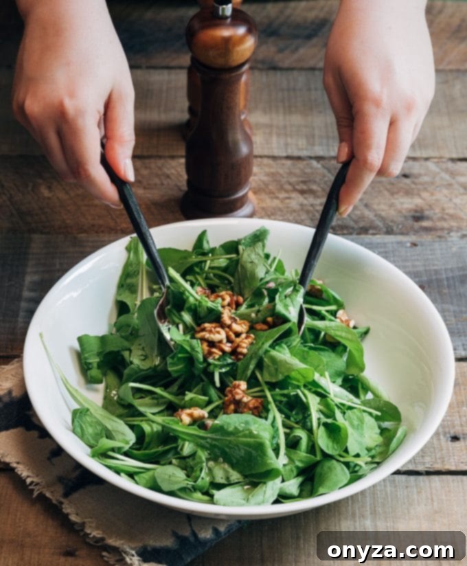 tossing baby arugula and walnuts with vinaigrette