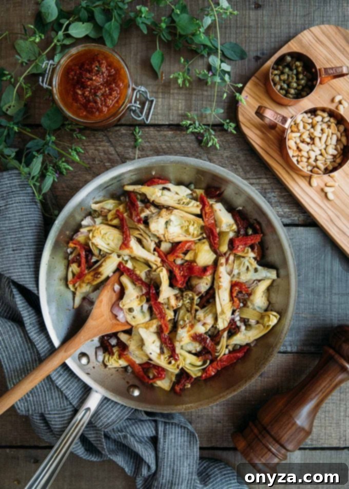 This Sun-Dried Tomato Pasta Salad recipe with sun-dried tomato vinaigrette, artichoke hearts, and Pecorino Romano cheese is easy to make and delicious! Perfect for a summer side dish or meatless dinner! #pasta #salad #pastasalad #sundriedtomatoes #vegetarian #easyrecipe sauteed artichokes and sun dried tomatoes in a saute pan