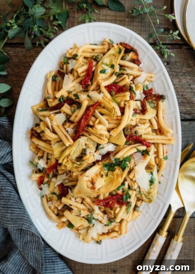 This Sun-Dried Tomato Pasta Salad recipe with sun-dried tomato vinaigrette, artichoke hearts, and Pecorino Romano cheese is easy to make and delicious! Perfect for a summer side dish or meatless dinner! #pasta #salad #pastasalad #sundriedtomatoes #vegetarian #easyrecipe artichoke pasta salad recipe with sun-dried tomato vinaigrette on a white serving platter