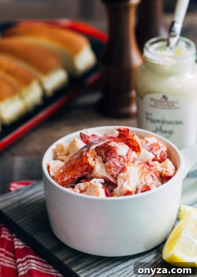 Freshly cooked lobster meat, cut into sizable chunks, gently mixed with creamy mayonnaise in a glass bowl, ready to be assembled into classic Maine lobster rolls.
