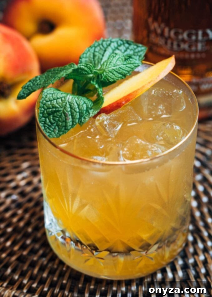 A chilled Bourbon Peach Smash cocktail garnished with fresh mint and a peach slice, perfect for summer.
