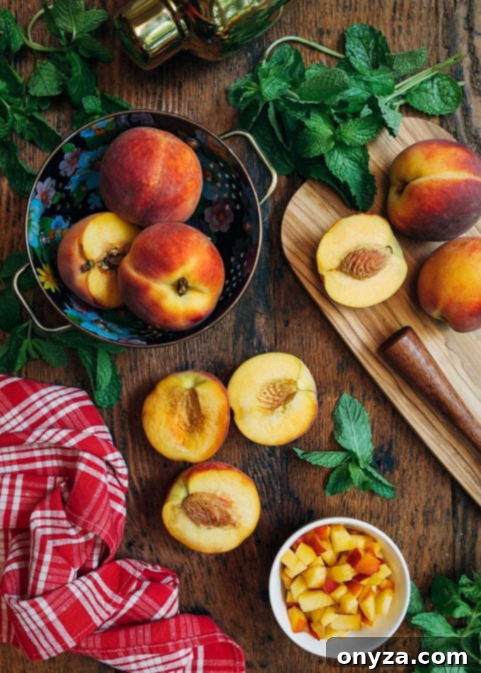 Fresh whole and sliced peaches arranged on a wooden board with vibrant green mint leaves, ready for muddling into a smash cocktail.