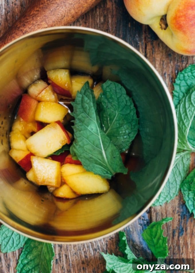 Diced peaches and fresh mint leaves are placed in a cocktail shaker, ready to be muddled for a Bourbon Peach Smash.