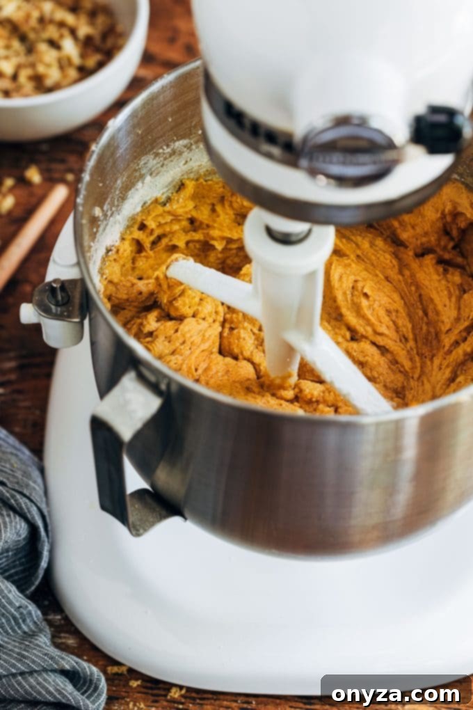 Rich pumpkin bread batter being mixed in a KitchenAid stand mixer, ready to be poured into loaf pans.