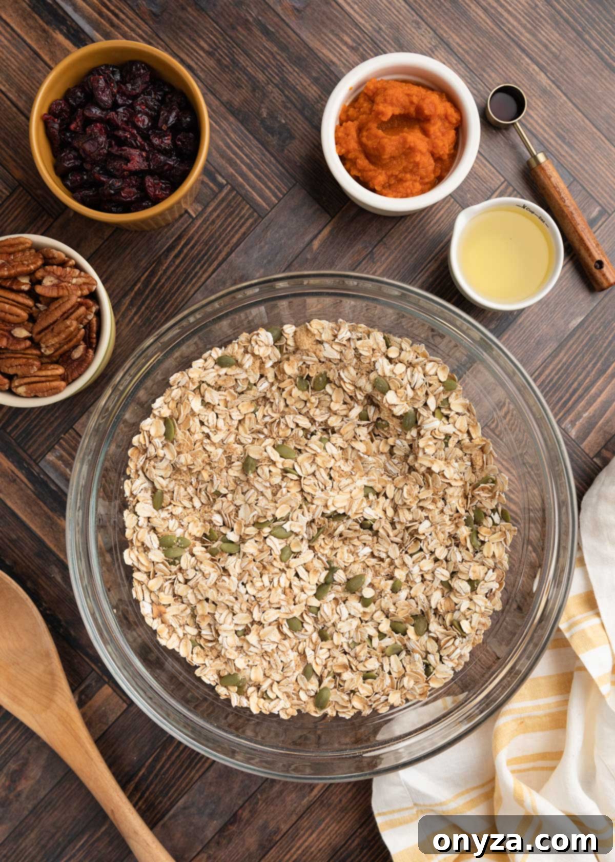 Overhead photo of dry granola ingredients meticulously mixed in a glass bowl on a warm wooden background, ready for the wet mixture.