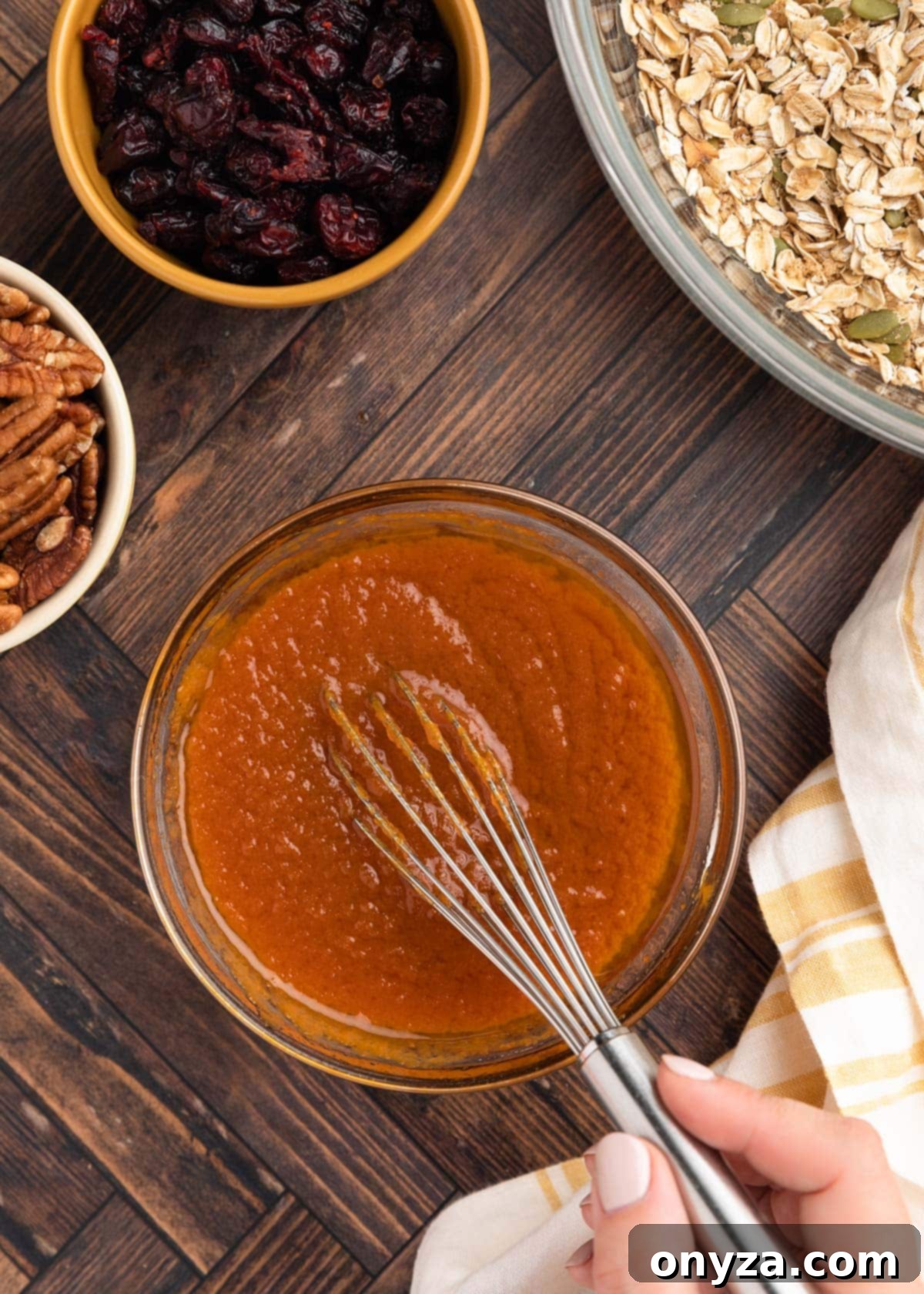 Overhead photo of creamy pumpkin puree being smoothly combined with oil, maple syrup, and vanilla extract using a whisk, creating the wet base.