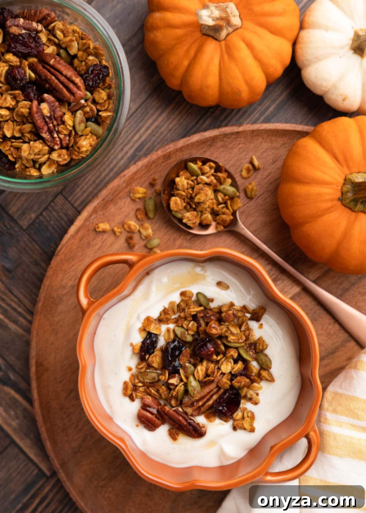 Overhead photo of pumpkin granola sprinkled generously over creamy yogurt in a charming pumpkin cocotte, a perfect fall breakfast or snack.