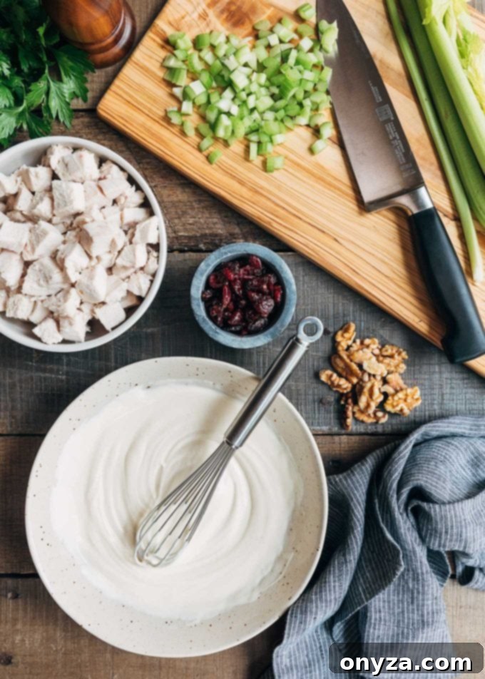 Ingredients for Cranberry Walnut Chicken Salad laid out on a rustic wood board, including dried cranberries, celery, shallots, parsley, and walnuts.