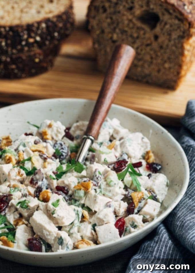 A large bowl of creamy cranberry walnut chicken salad, with a serving spoon resting inside, ready to be enjoyed.