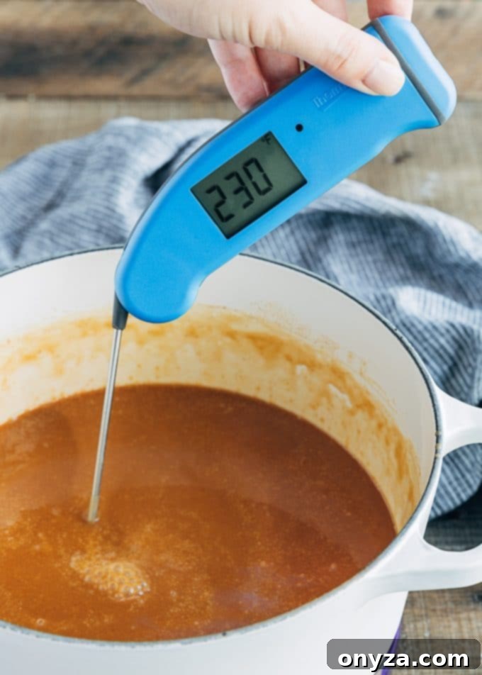 An instant-read thermometer accurately measuring the temperature of the simmering apple cider caramel in a pot.