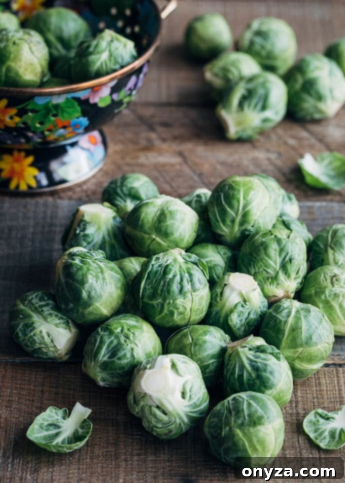 Fresh, raw Brussels sprouts on a rustic wooden board next to a colander, ready for preparation.