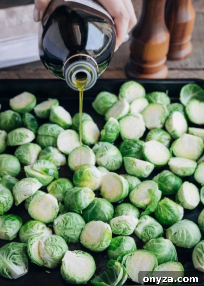 Pouring olive oil over halved Brussels sprouts on a baking pan, preparing them for roasting.