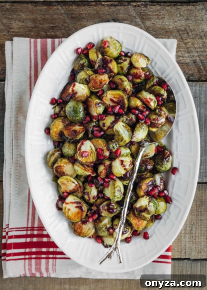 A festive serving dish filled with roasted Brussels sprouts, garnished with bright red pomegranate arils and a luscious glaze.