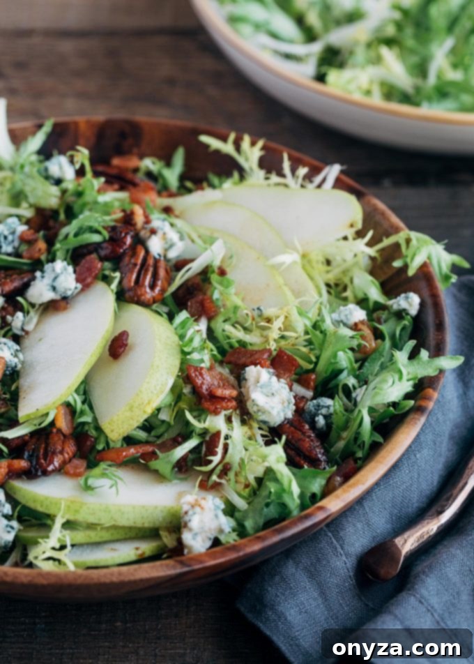 Beautifully plated frisée salad with sliced pears, pecans, and a generous drizzle of warm maple bacon vinaigrette in a elegant serving bowl