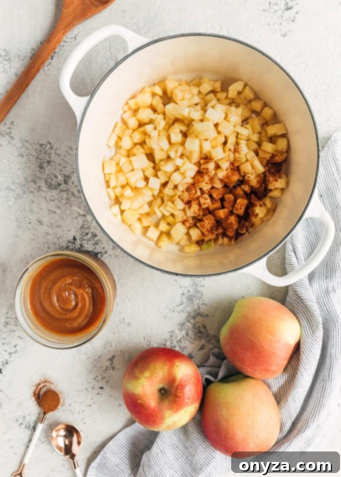 Diced Fuji apples in a pot, ready for cooking, with a bowl of homemade caramel sauce and whole apples beside