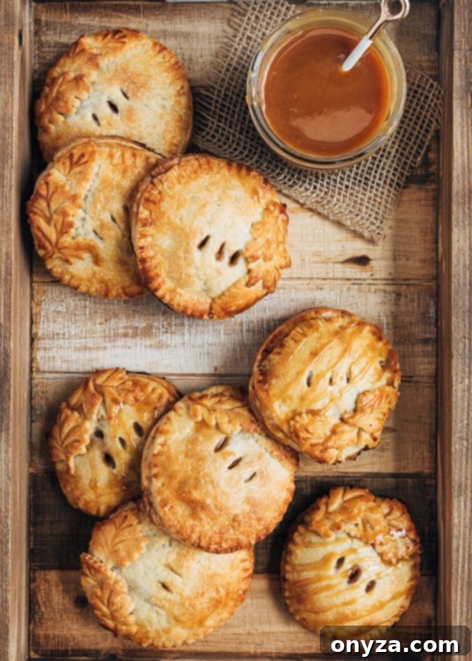 A rustic wooden tray laden with warm caramel apple hand pies, accompanied by an inviting bowl of caramel sauce for drizzling