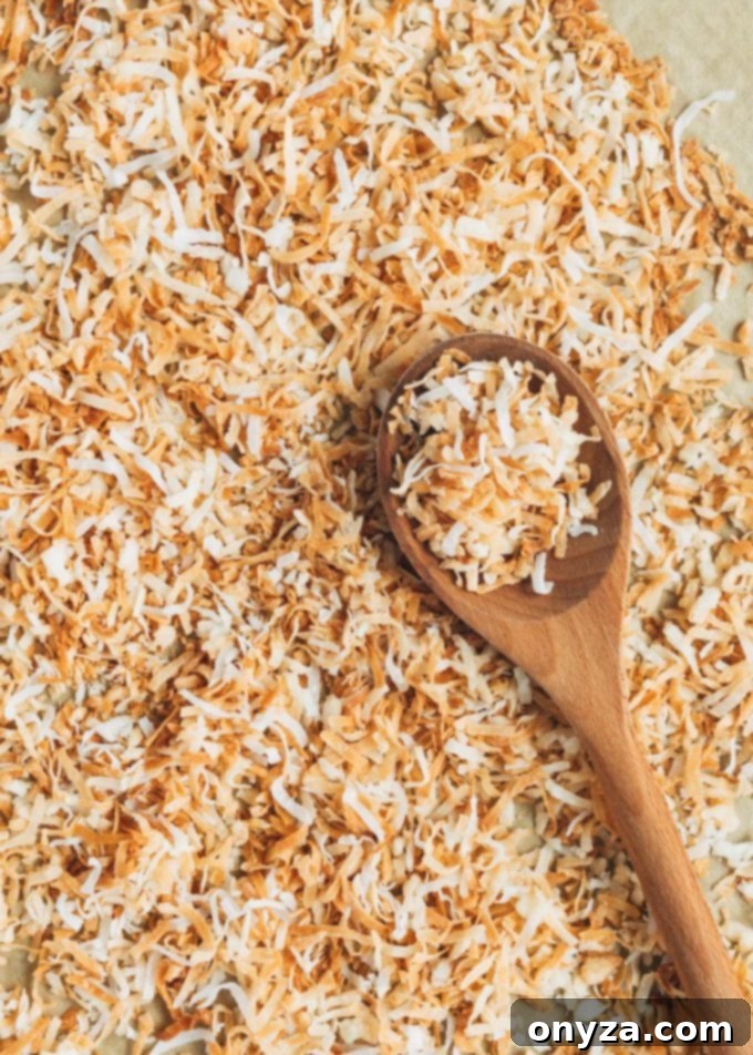 toasted coconut flakes on a sheet pan with a wooden spoon
