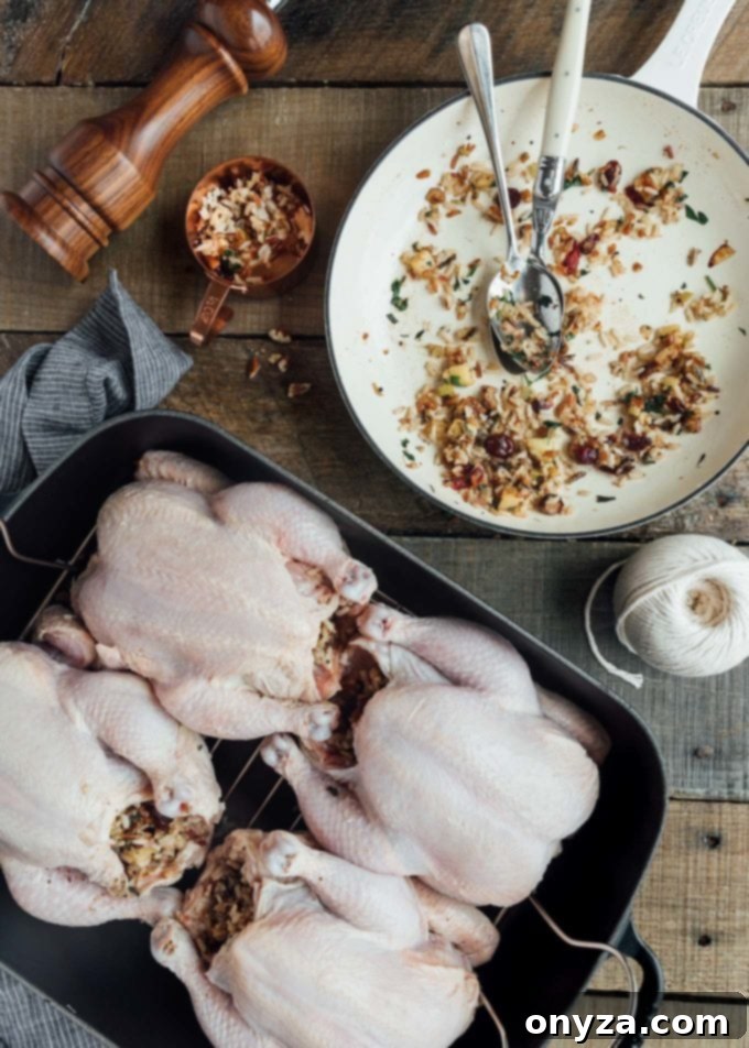 Several stuffed Cornish game hens roasting in a metal pan, with an additional pan of rice stuffing beside them.