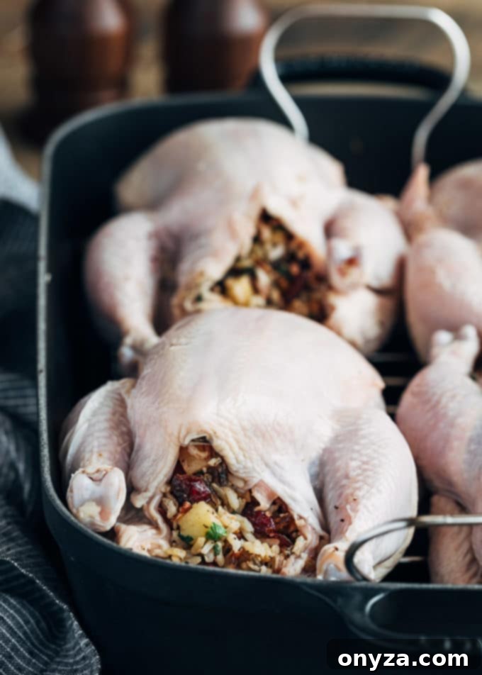 Four partially glazed stuffed Cornish hens cooking on a roasting rack in a baking pan.