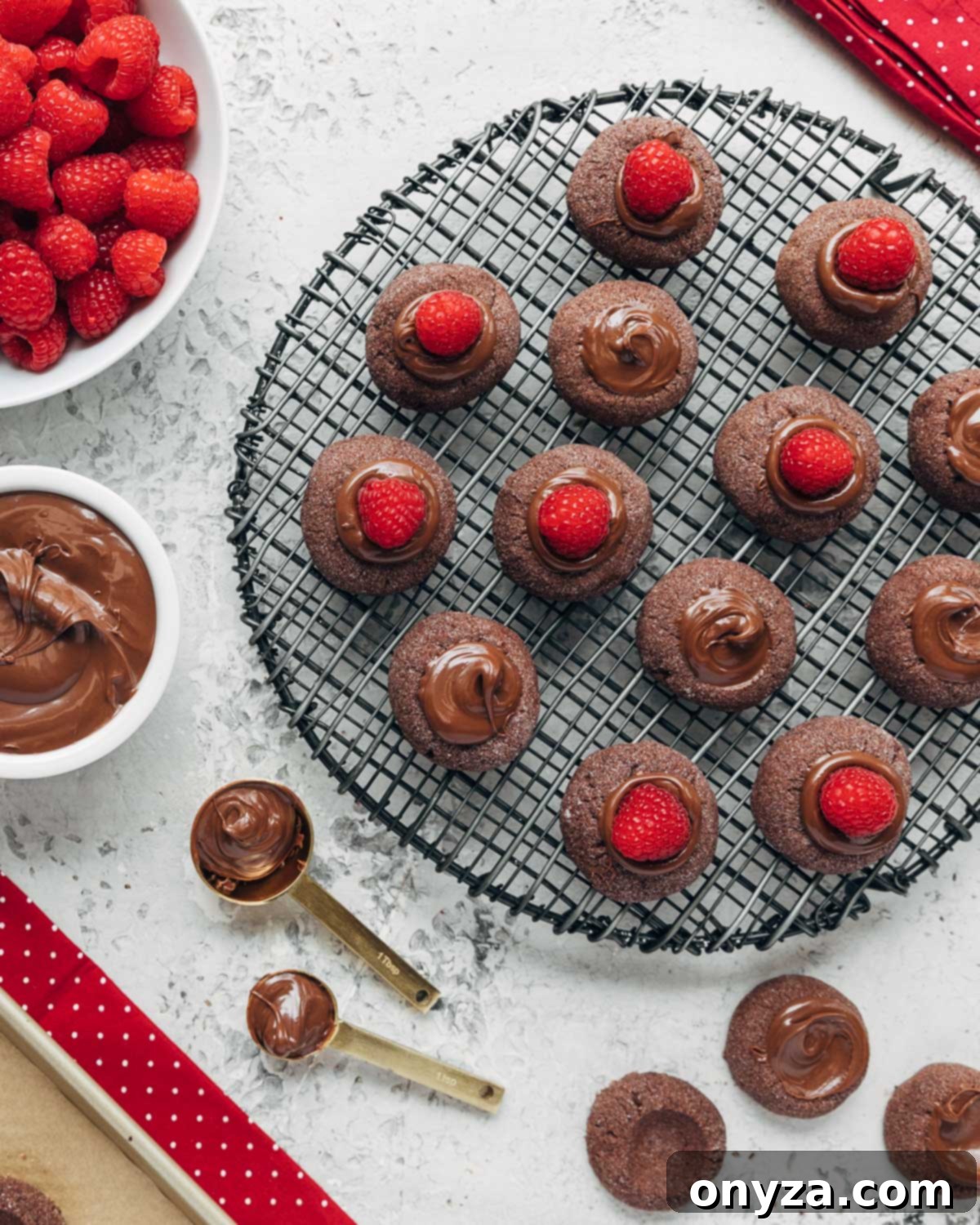 filled chocolate hazelnut thumbprint cookies on a cooling rack with bowls of raspberries and chocolate hazelnut spread