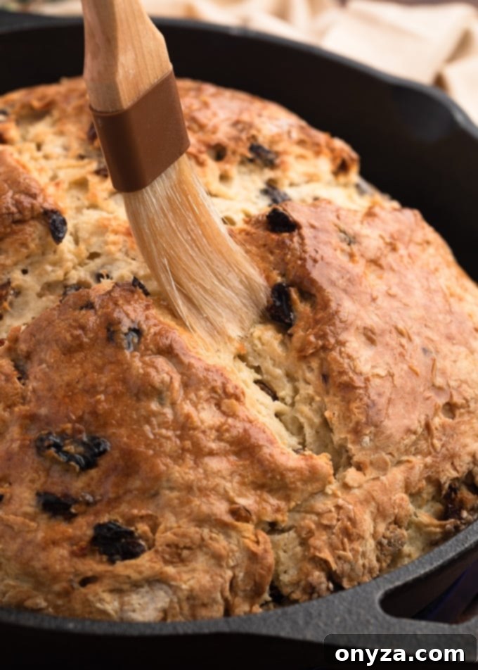 Classic Irish-American Soda Bread 7 brushing melted butter onto baked soda bread in a cast iron skillet