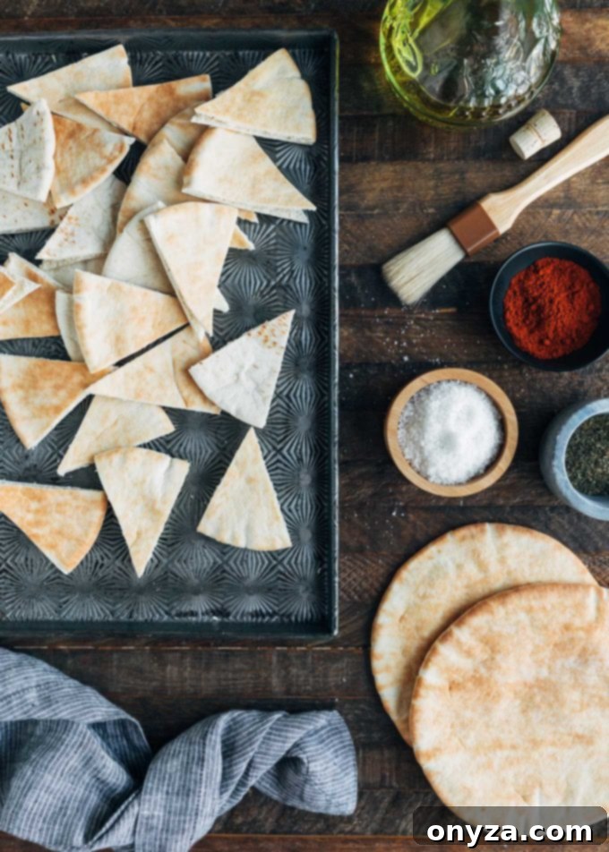 cut pita wedges arranged on a baking sheet, ready for seasoning and baking, with small bowls of various spices