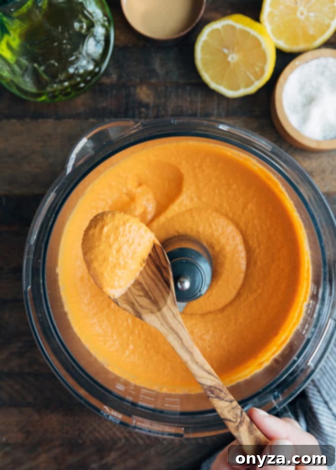 spoonful of roasted red pepper hummus held over a food processor bowl