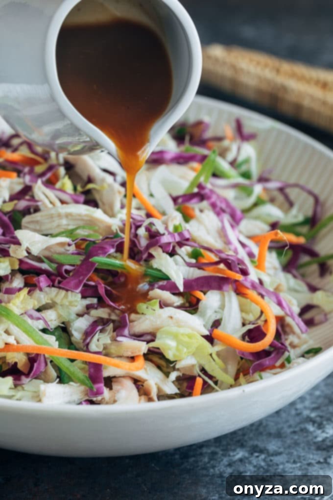 pouring plum vinaigrette over tossed chicken salad in a large bowl