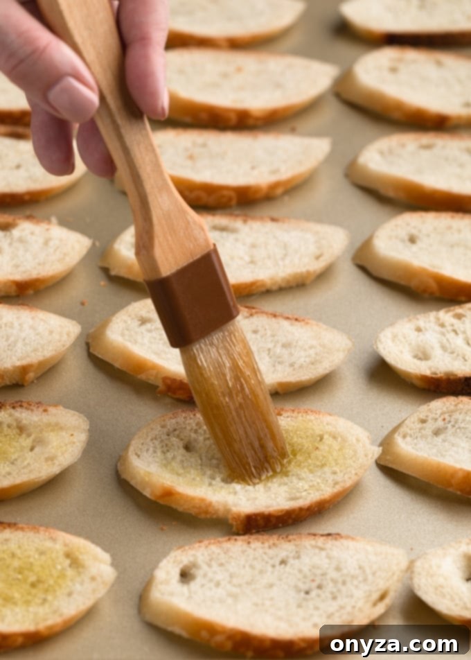 pastry brush with olive oil on sliced baguette