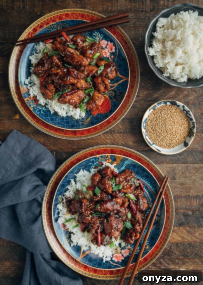 Overhead view of two plates of General Tso's Chicken served over white jasmine rice, garnished with green scallions and sesame seeds