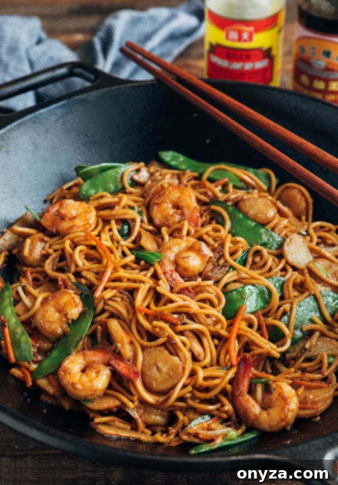 Shrimp Lo Mein 5 Shrimp lo mein cooking in a wok, with vibrant snow peas and carrots visible among the noodles and shrimp.