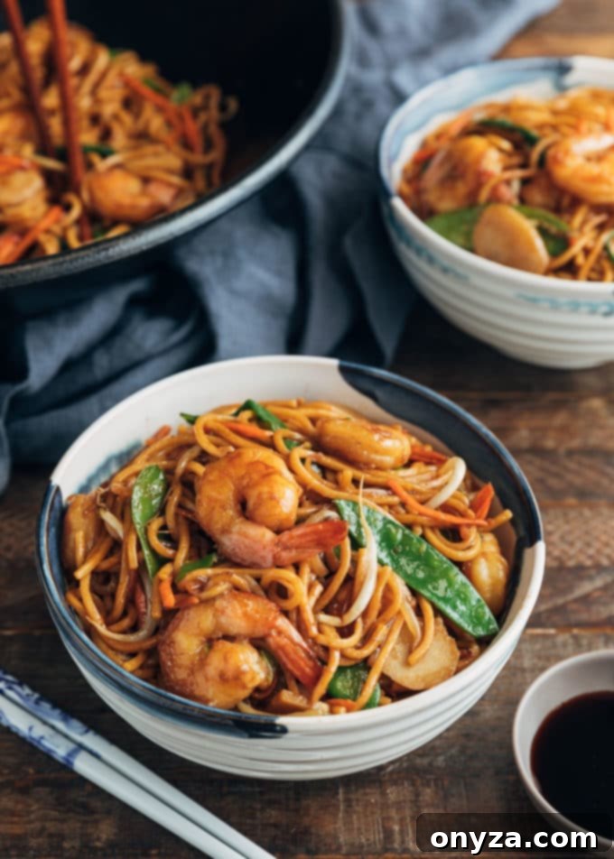 Shrimp Lo Mein 6 Two bowls of shrimp lo mein served hot, with a small dish of soy sauce on the side for custom seasoning.