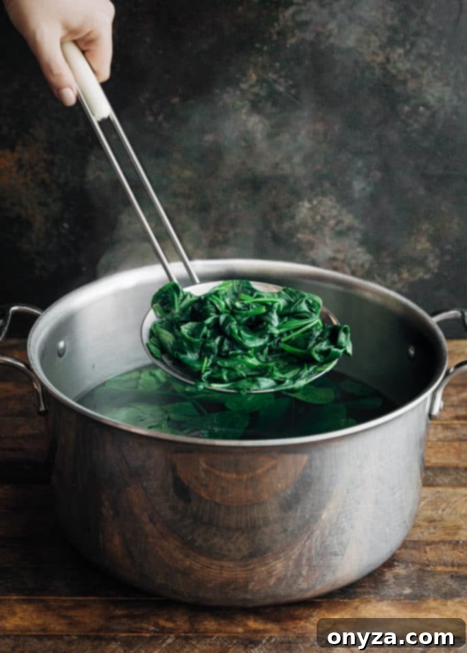 Blanched baby spinach leaves being strained in a colander over a pot, with ice bath ready in the background.