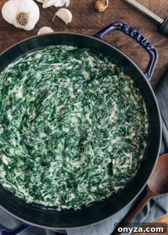 Finished creamed spinach in a red Staub pot, garnished with a sprig of parsley.