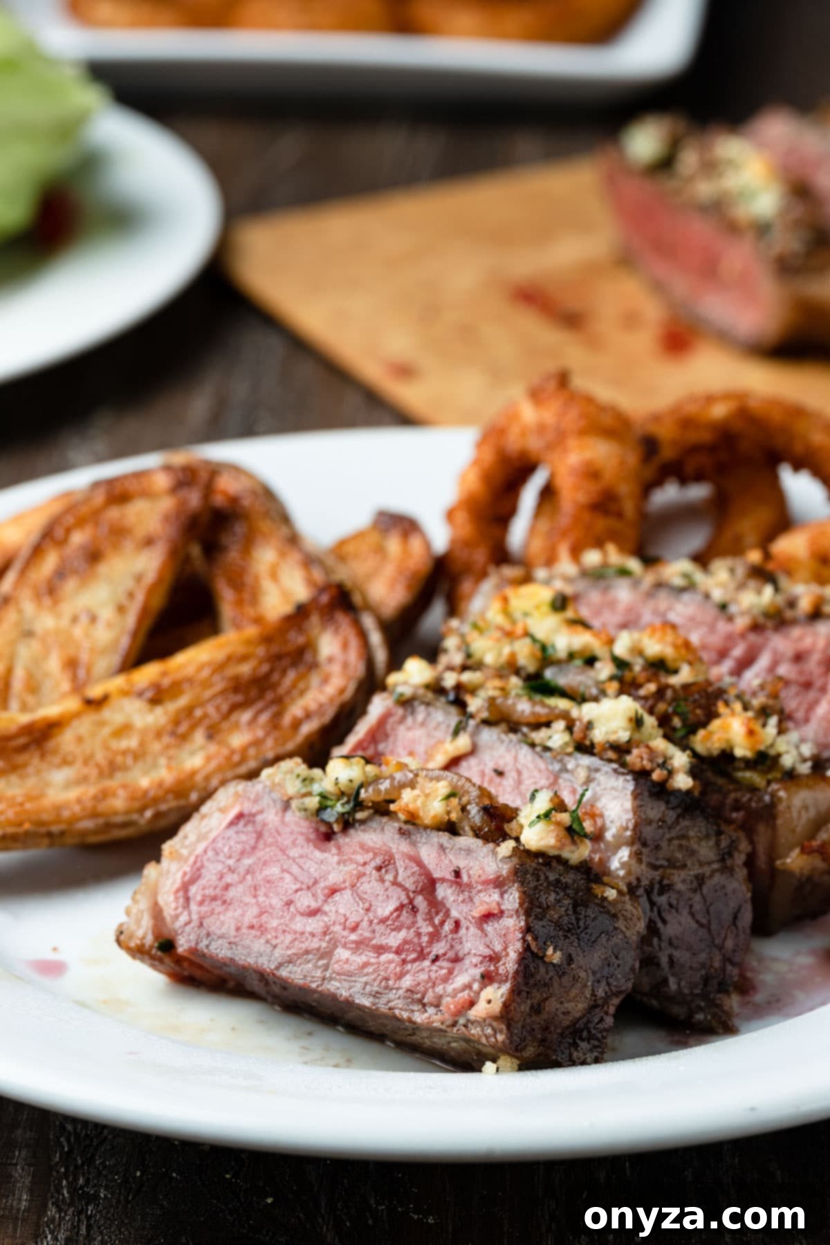 Balsamic Shallot Steak with Blue Cheese Crust 2 blue cheese crusted new york strip steak on a white plate with french fries and onion rings