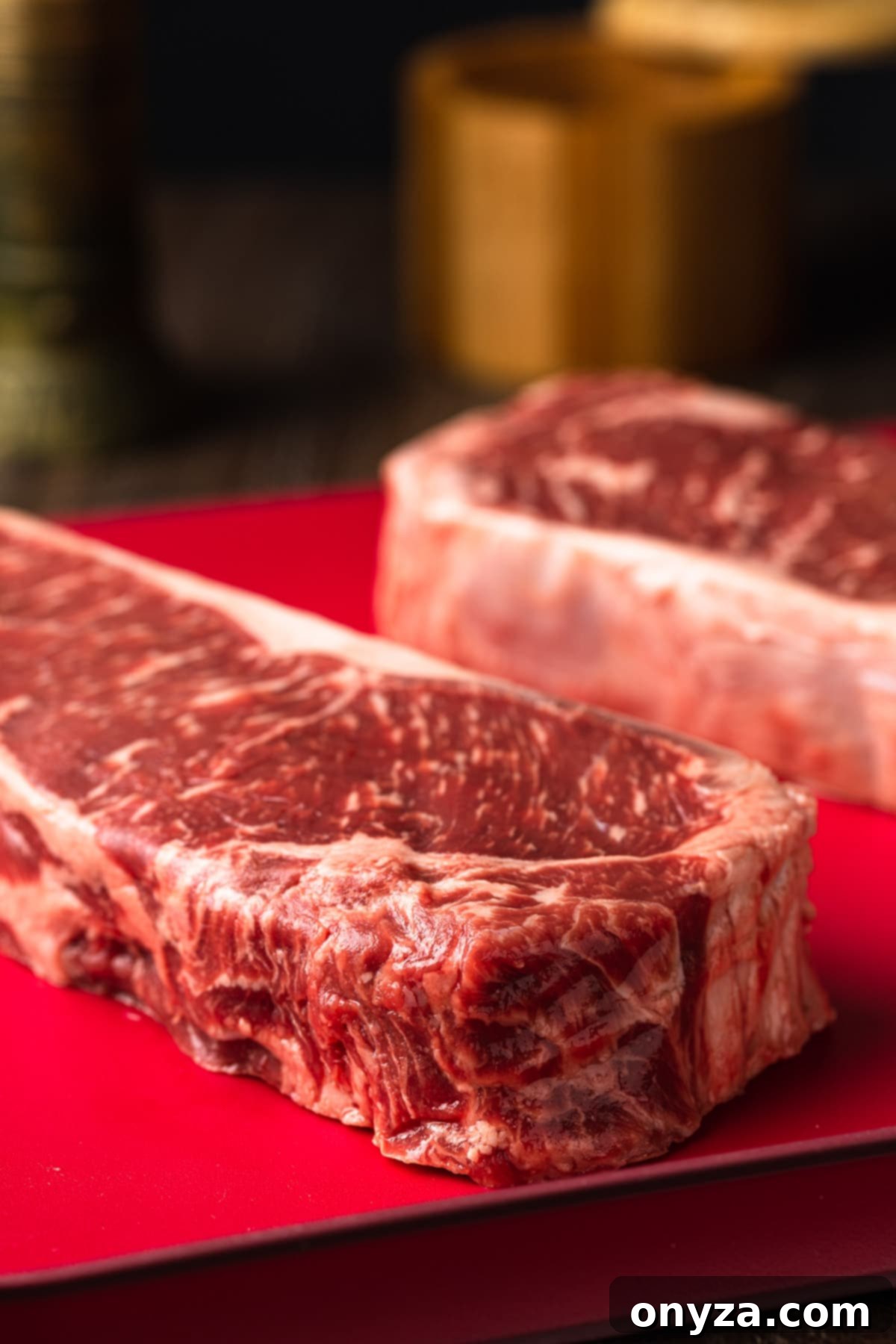 Balsamic Shallot Steak with Blue Cheese Crust 3 uncooked new york strips steaks on a red cutting board