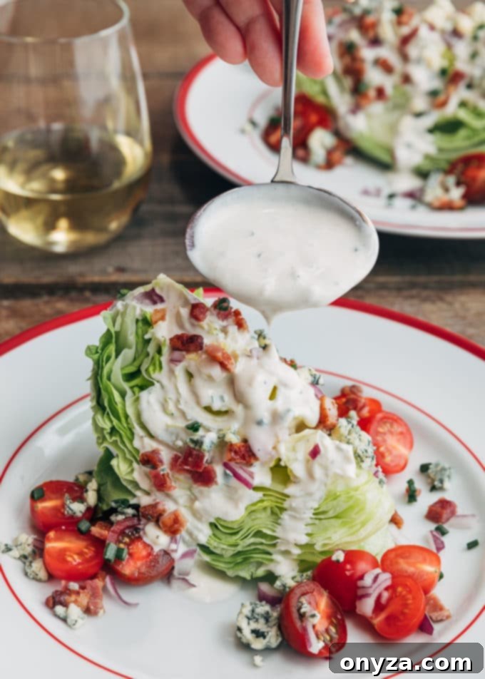 A generous ladleful of creamy blue cheese dressing being poured over a meticulously prepared Classic Wedge Salad, showcasing the dressing cascading over crisp iceberg lettuce, savory bacon, and fresh tomatoes.