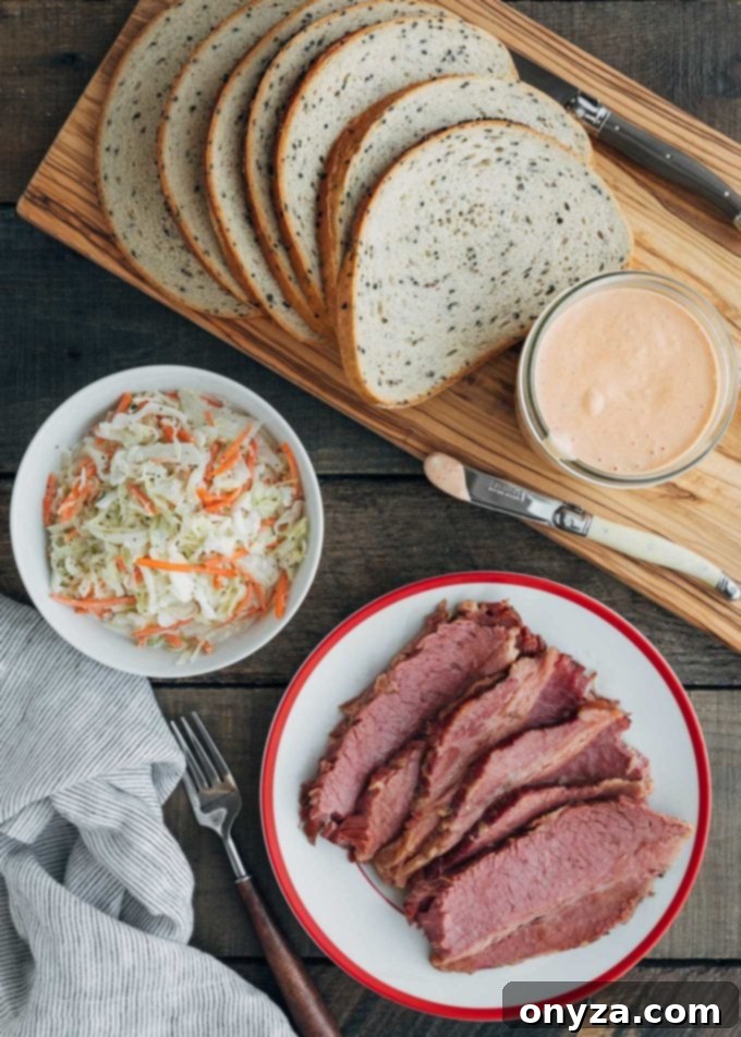 Sliced corned beef on a plate next to a bowl of coleslaw and a loaf of seeded rye bread, essential ingredients for the perfect sandwich