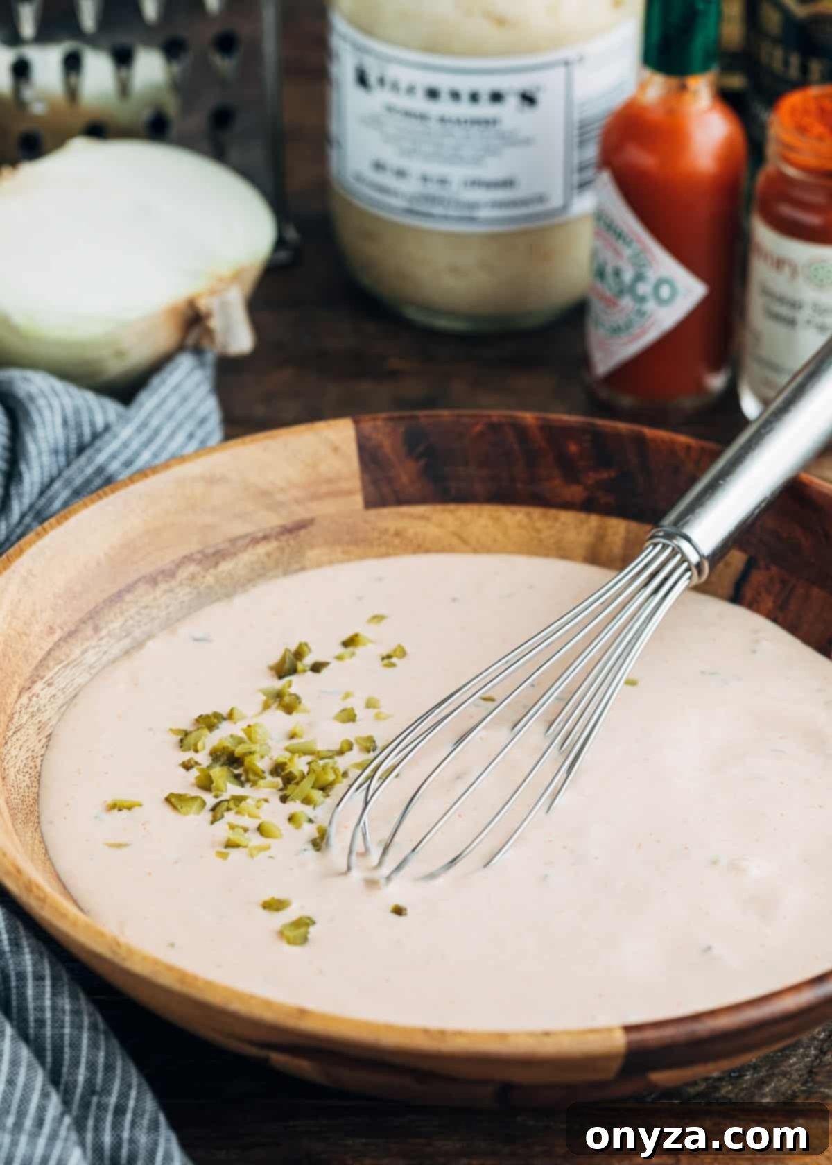 Mixed homemade Russian dressing in a wooden bowl with a whisk, showing a few chopped cornichons on top