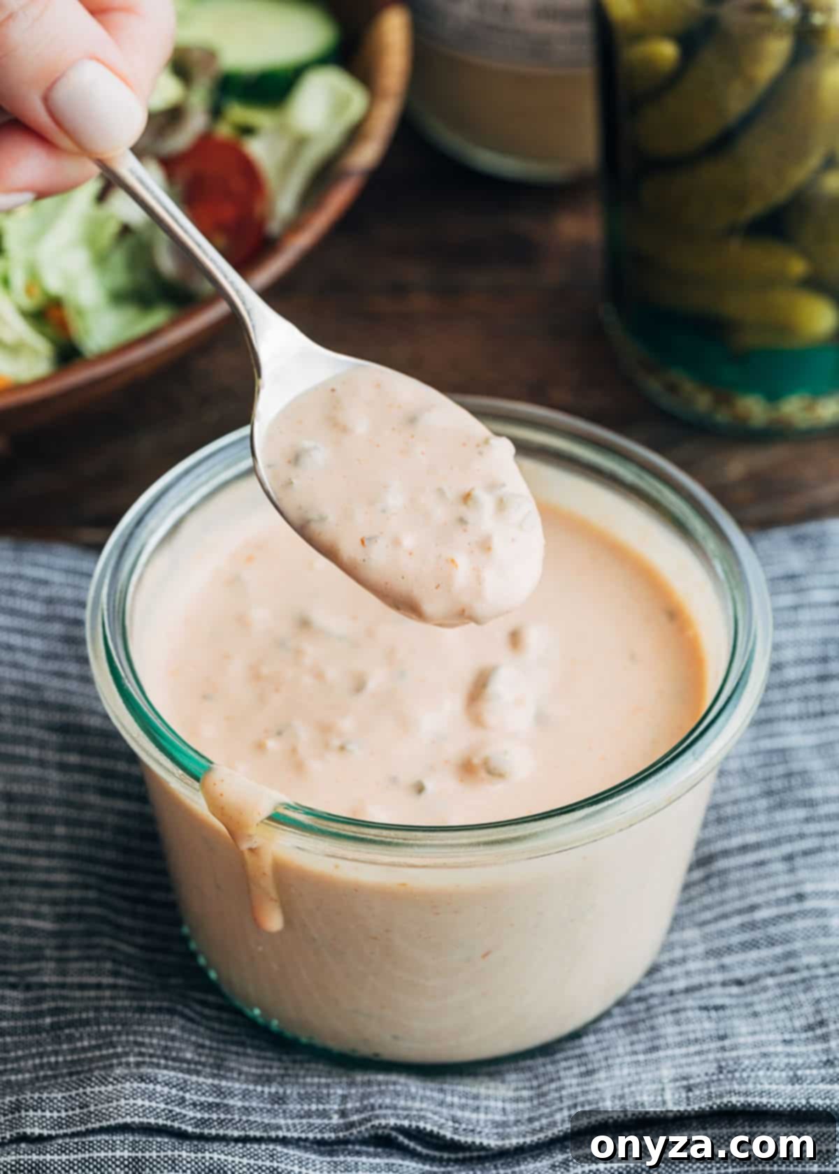 A spoonful of homemade Russian dressing being lifted from a glass jar