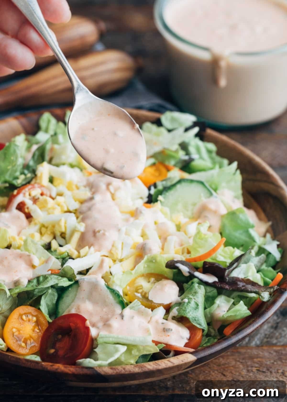 Homemade Russian dressing being drizzled over a vibrant house salad with a spoon