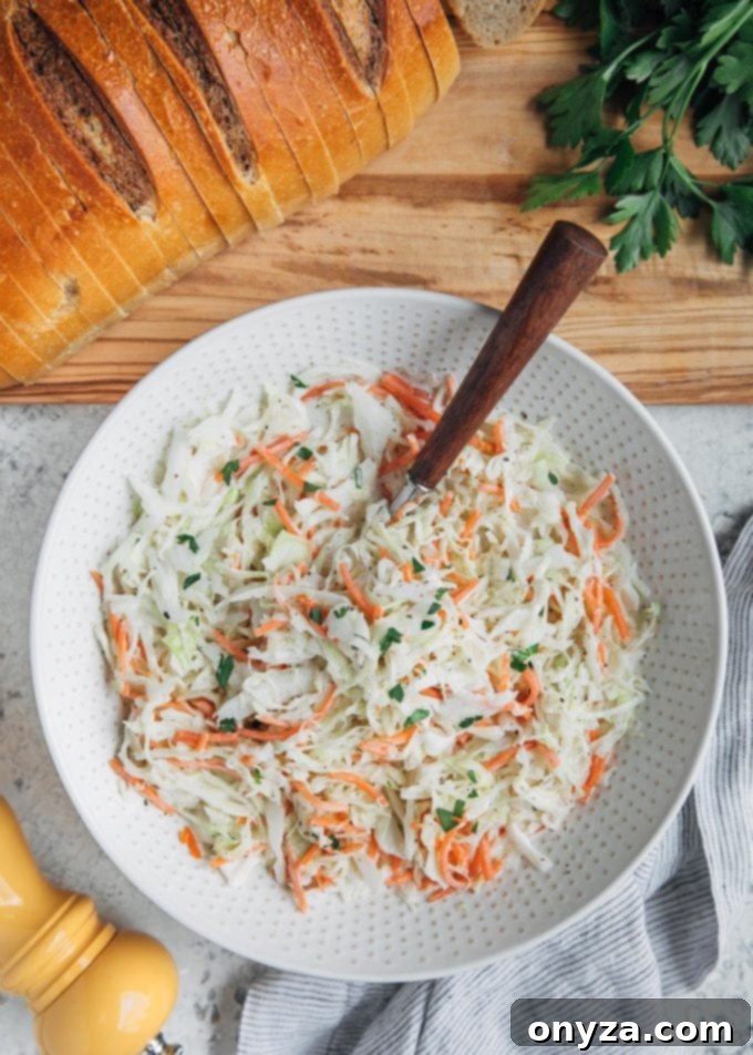 Creamy Homemade Deli Coleslaw 6 A bowl of deli-style homemade coleslaw served alongside slices of rye bread, highlighting its perfect pairing for sandwiches and meals.