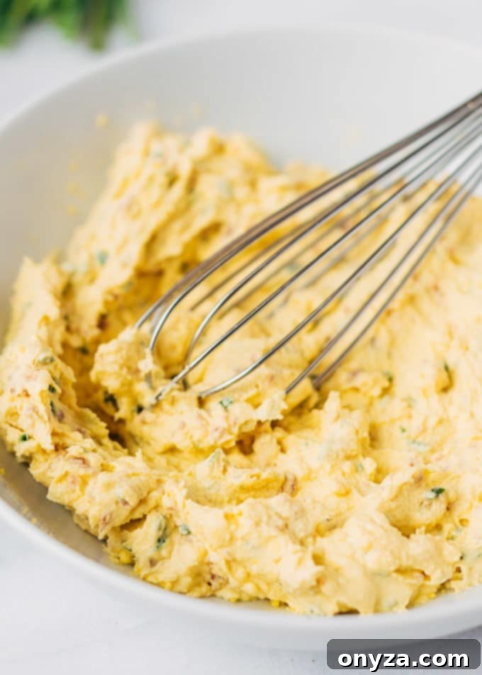 Zesty Horseradish Bacon Deviled Eggs 4 bacon deviled egg filling in a bowl with a whisk