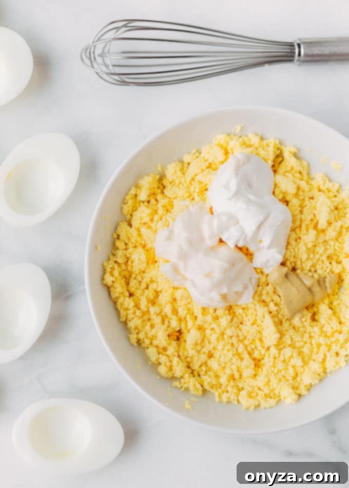 hard boiled egg yolks in a bowl with mayonnaise, sour cream, and Dijon mustard